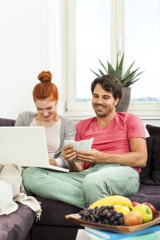 Close up Young Couple Resting at the Couch with Laptop Computer, ATM Card and Euro Cash.