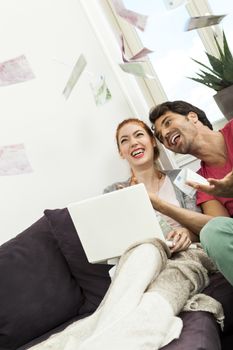 Close up Very Happy Young Couple with Laptop Sitting at the Couch and Throwing Euro Money in the Air.