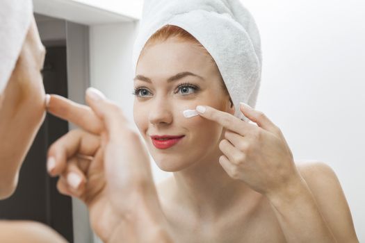 Close up Fresh Woman After Shower Applying White Cream on her Face in Front a Mirror With Towel on her Head.