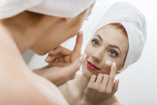 Close up Fresh Woman After Shower Applying White Cream on her Face in Front a Mirror With Towel on her Head.