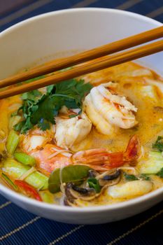 Bowl of traditional Thai tom yam soup with vegetables and prawns in a spicy aromatic broth served with chopsticks