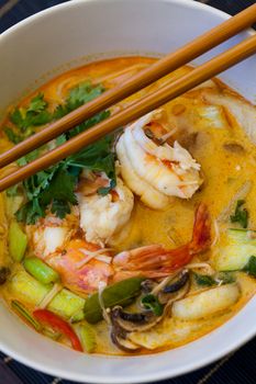 Bowl of traditional Thai tom yam soup with vegetables and prawns in a spicy aromatic broth served with chopsticks