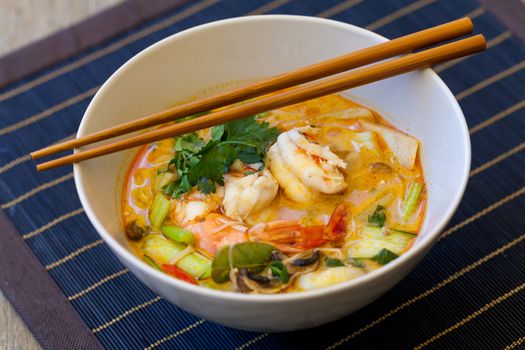 Bowl of traditional Thai tom yam soup with vegetables and prawns in a spicy aromatic broth served with chopsticks