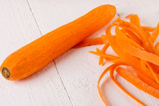 Fresh peeled carrots sliced into thin batons for carrot julienne with a metal kitchen cutter on a white background