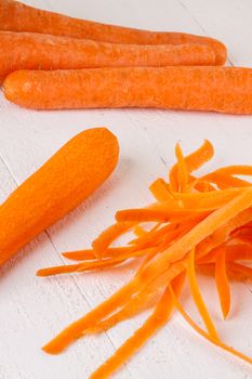 Fresh peeled carrots sliced into thin batons for carrot julienne with a metal kitchen cutter on a white background