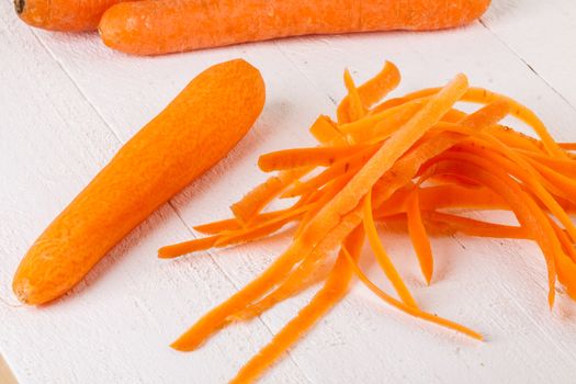 Fresh peeled carrots sliced into thin batons for carrot julienne with a metal kitchen cutter on a white background