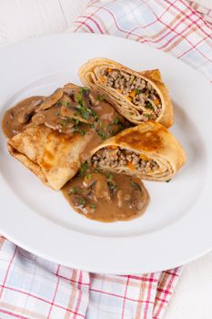 Savory mince pancakes or tortillas cut open to show the ground or minced meat and vegetable filling in a rich tasty gravy