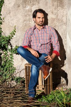 Smiling male model sitting on wooden crate with legs crossed