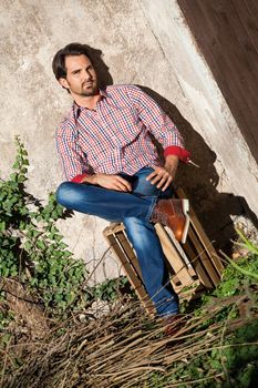 Smiling male model sitting on wooden crate with legs crossed