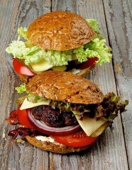 Tasty Homemade Hamburgers with Roasted Beef, Lettuce,Tomato, Onions, Cheese, Bacon and Pickle on Whole Wheat Bun closeup on Rustic Wooden background