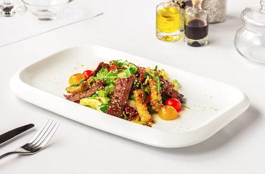 Warm salad with beef and vegetables on a rectangular white plate. served on a white table