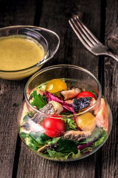 fresh salad of red fish, lettuce and tomatoes. Salad, sauce and fork on a wooden table