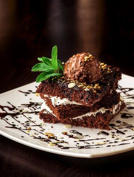 Chocolate brownie cake with a scoop of ice cream with a mint leaf on a white plate