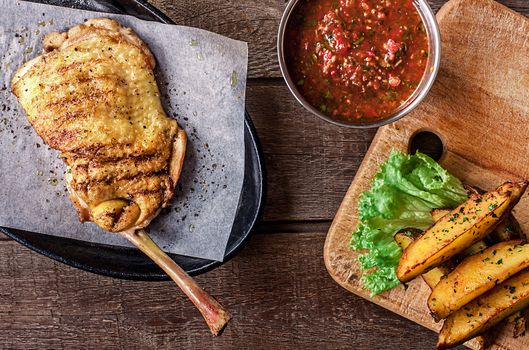 Fried chicken meat on the bone, red sauce, potato wedges, lettuce on background wooden table