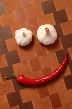 two heads of garlic and chili pepper on a chopping board