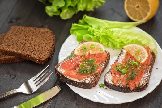 Homemade sandwich with salmon and rye bread , butter lemon, and lettuce for breakfast