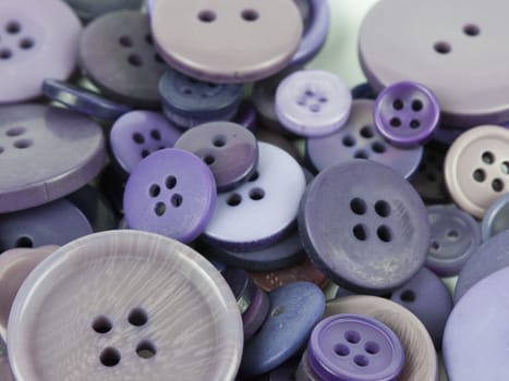 Close up of various purple button scattered on a white surface.