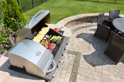 Grilling healthy food with corn, kebabs, meat and sausages on an outdoor gas barbecue on a luxury brick paved patio and summer kitchen in a neatly manicured back yard