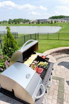 Food arranged ready for grilling on an outdoor gas barbecue in a summer kitchen on a brick paved outdoor patio with a view of a lake in a healthy lifestyle concept