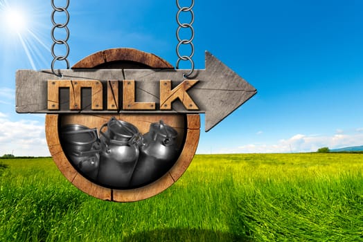 Wooden sign with directional arrow with text Milk and steel cans for the transport of milk. Hanging from a metal chain in a countryside landscape