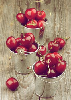 Ripe Sweet Cherries in Three Tin Buckets isolated on Rustic Wooden background. Retro Styled