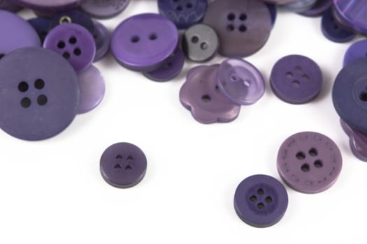 Close up of various purple button scattered on a white surface.