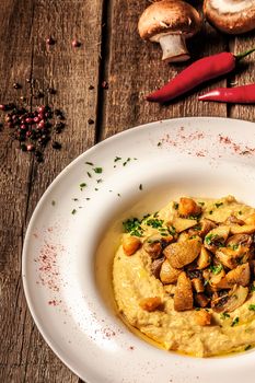 corn porridge with pumpkin  with mushrooms on white plate and wooden background