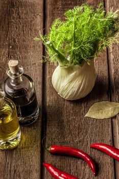 fresh fennel full of vitamins and fibers on wooden table. olive oil, balsamic vinegar, red pepper pods, bay leaves