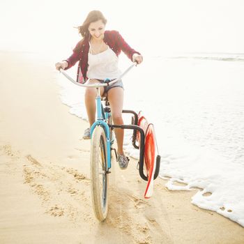 Surfer young woman riding her bicycle on the beach