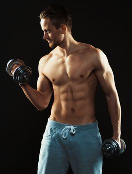 Athletic attractive man with dumbbells on the black background