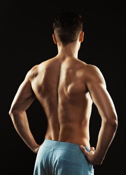 Young athletic man showing his back on the black background