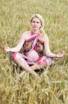 pregnant woman doing meditation in wheat field
