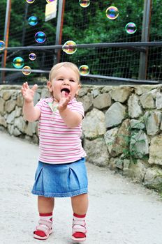 happy baby girl catching soap bubbles in the park 