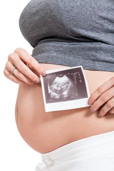 Pregnant woman displaying a prenatal ultrasound scan showing her unborn foetus in the womb against her swollen belly, isolated on white