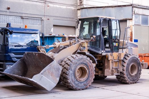 Front end loader with its bucket or scoop down parked in front of a warehouse on paving