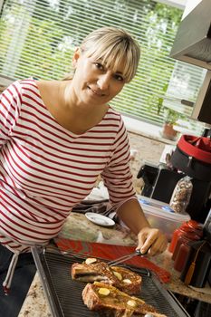 Attractive blond woman barbecuing meat outdoors in the garden grilling two marinated spicy beef steaks over a fire