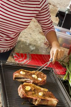 Attractive blond woman barbecuing meat outdoors in the garden grilling two marinated spicy beef steaks over a fire