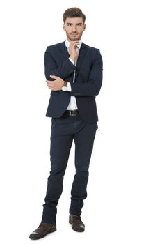 Stylish successful handsome young businessman standing in a relaxed pose with his hands in his pockets and his suit jacket open, isolated on white