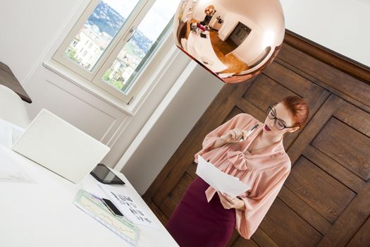 Serious Young Office Woman Writing a Document on Top of her Desk While in Standing Position.