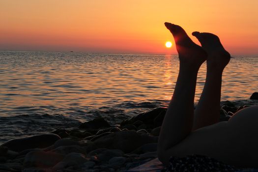 Naked woman legs and evening beach on the sunset