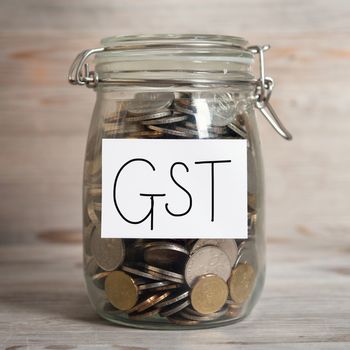 Coins in glass money jar with gst label, financial concept. Old wooden background with dramatic light.