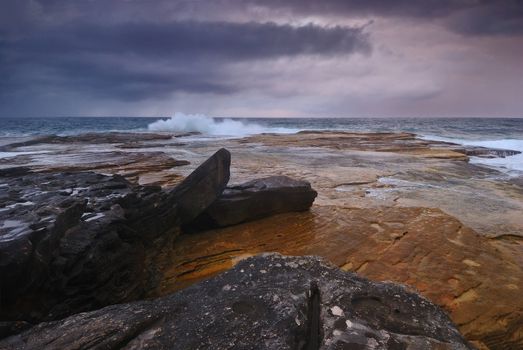 Rocky seascape sunrise scene with distant ocean and colored rocks on the foreground