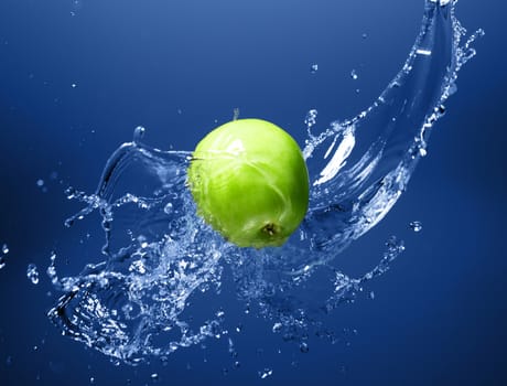 Green apple with water splash on blue water background