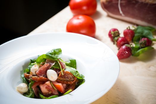 Salad with strawberry, prosciutto, herbs, cottage cheese and blackberry balsamic vinegar. Shallow dof.