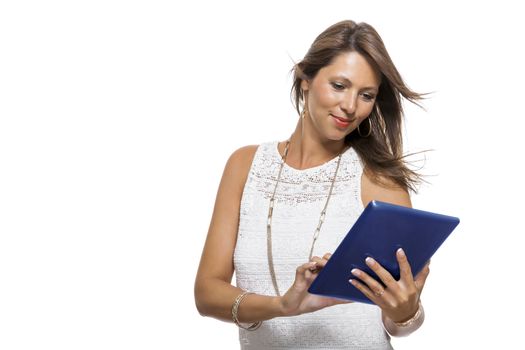 Attractive young business woman standing chatting on a mobile while simultaneously reading a tablet computer with a smile, isolated on white