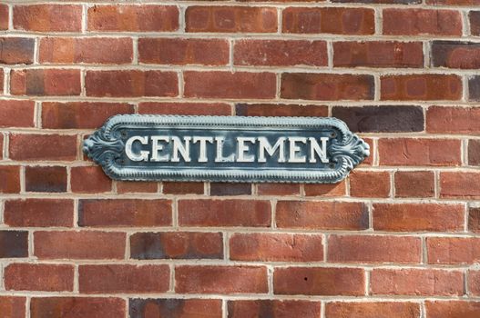 Old vintage gentlemen restroom sign on red brock wall in urban area.