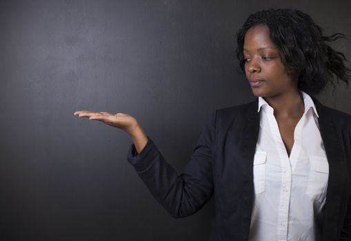 South African or African American woman teacher or student with hand out on chalk black board background