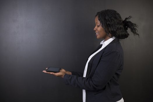 South African or African American woman teacher or student holding computer tablet on blackboard background