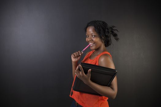 South African or African American woman teacher or student with notepad and pen against a blackboard background