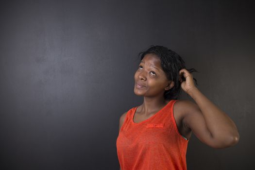 South African or African American woman teacher thinking scratching head on chalk black board background